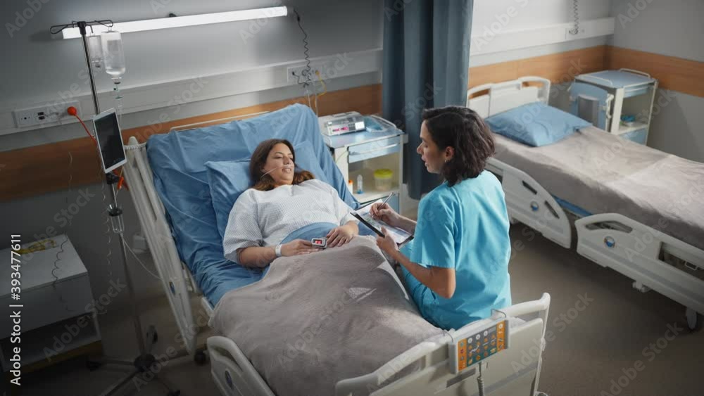 Hospital Ward: Friendly Hispanic Head Nurse Fills Medical History Form, Talks to Female Patient Recovering in Bed. Professional Nurse Helps Happy Woman Get Better after Surgery. Descending Shot Hospital Ward: Friendly Hispanic Head Nurse Fills Medical History Form, Talks to Female Patient Recovering in Bed. Professional Nurse Helps Happy Woman Get Better after Surgery. Descending Shot