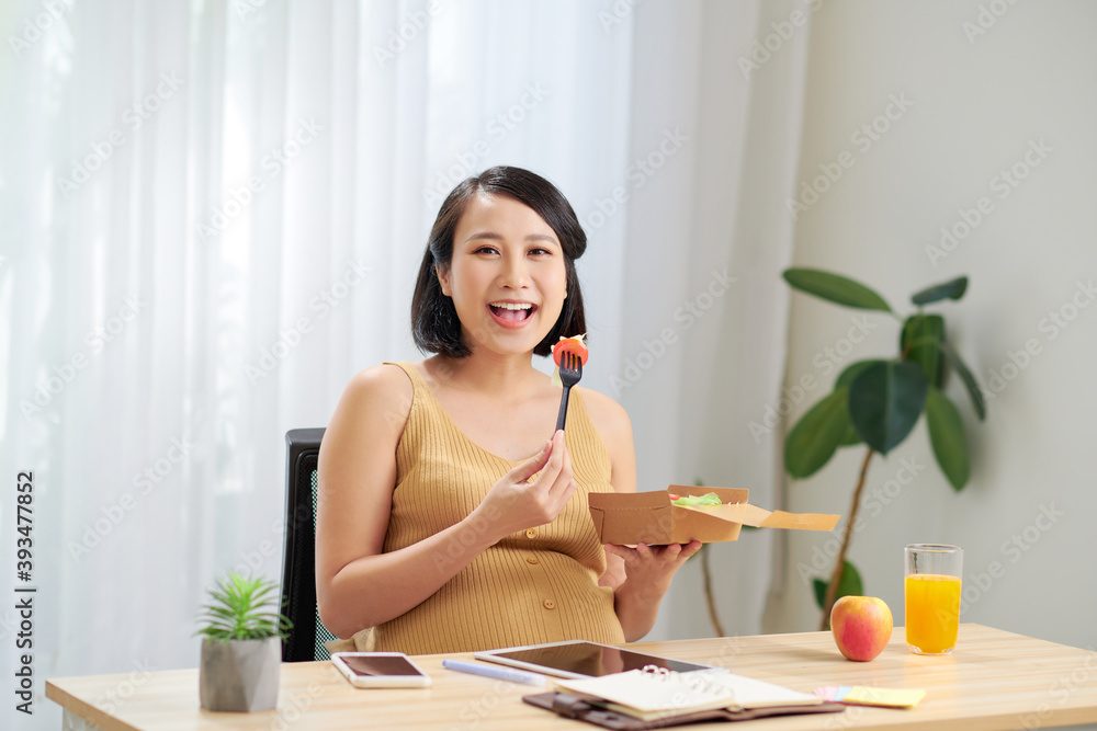 A young pregnant woman standing in home office and using tablet pc. Breakfast time.