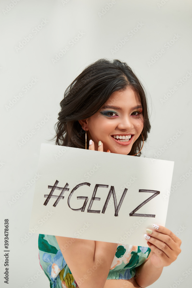 Young millennial teenage with a funny expression, holds a sign with the text Young millennial teenage with a funny expression, holds a sign with the text