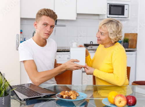 Happy mature woman taking white box from her adult son at kitchen