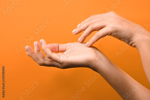 Cropped view of tender hands with pastel manicure touching each other with fingers, isolated on orange background with copy space