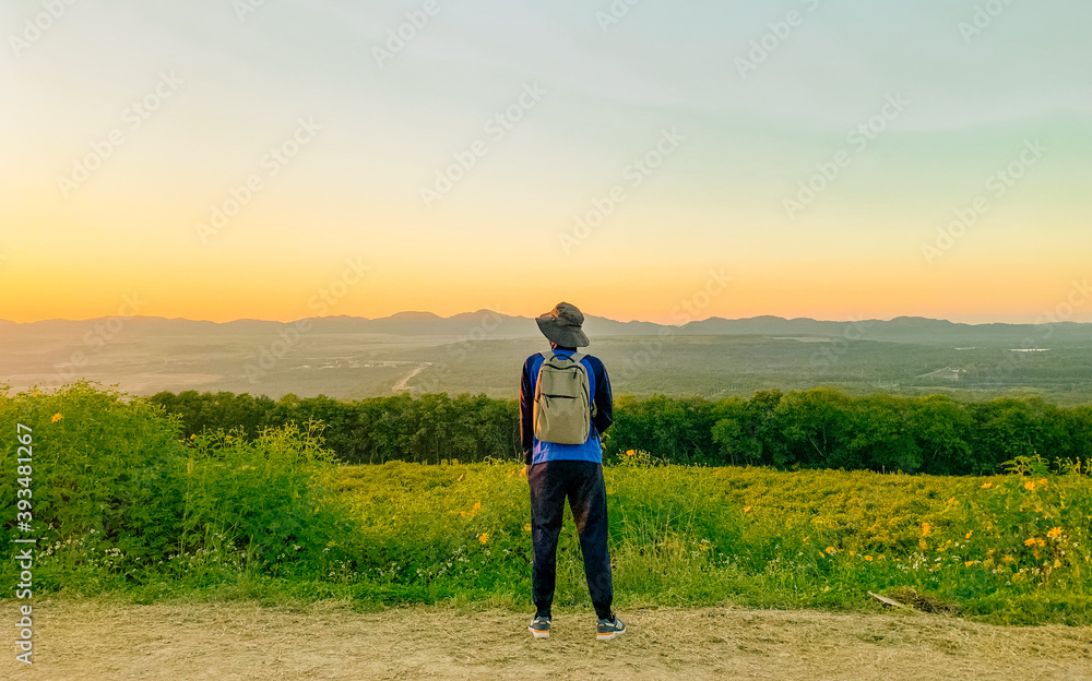 Young man asian traveler looking view sunset on Tung Bua Tong, Mae Moh, Lampang, Thailand. Mexican sunflower field. Travel concept