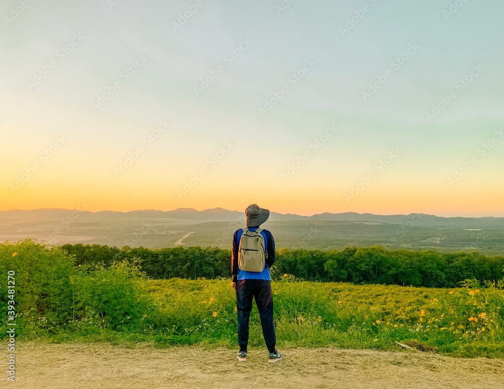 Young man asian traveler looking view sunset on Tung Bua Tong, Mae Moh, Lampang, Thailand. Mexican sunflower field. Travel concept
