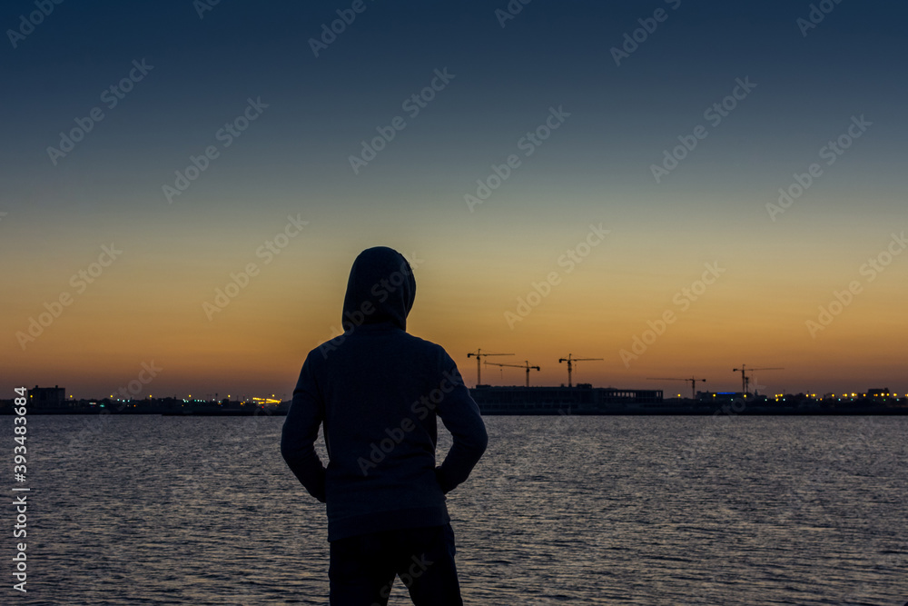 Fototapeta premium A man wearing jacket with hat watching sun rising from sea at the corniche park in Dammam, Kingdom Saudi Arabia