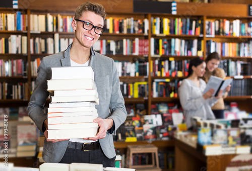 Handsome positive young man holding pile of books bought in bookstore