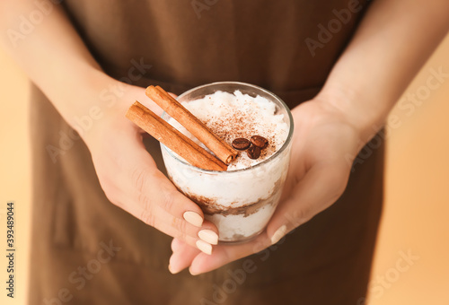 Woman holding glass of tasty rice pudding with cinnamon on light background