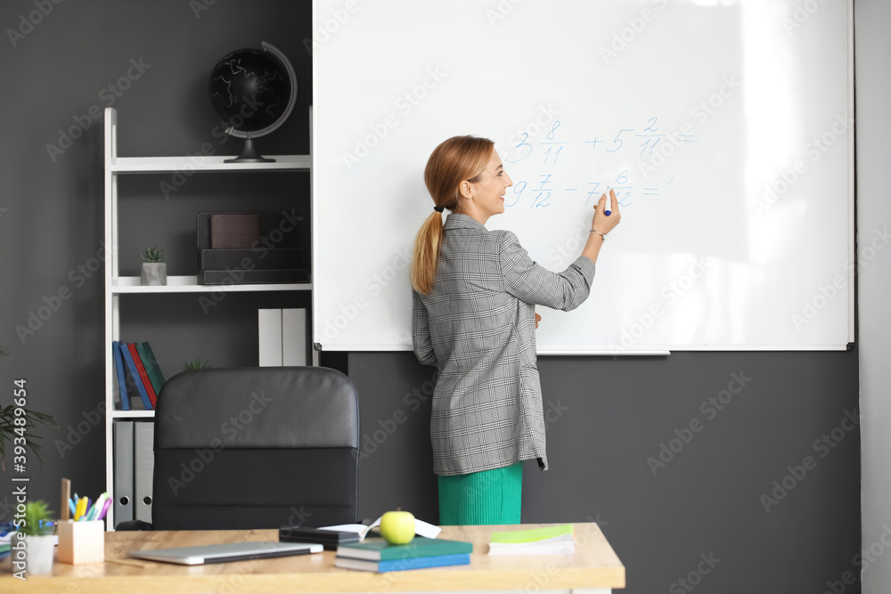 Mature maths teacher near blackboard in classroom Mature maths teacher near blackboard in classroom