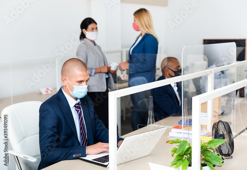 Manager wearing a protective mask works with other workers in a modern office © JackF