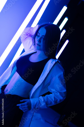 Portrait trendy young female dancer posing in the studio on a colorful background with neon lighting tube. Fashion street wear.