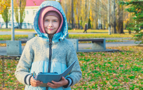 A young girl stands against the background of an autumn landscape, holds a tablet in her hands and looks into the camera photo