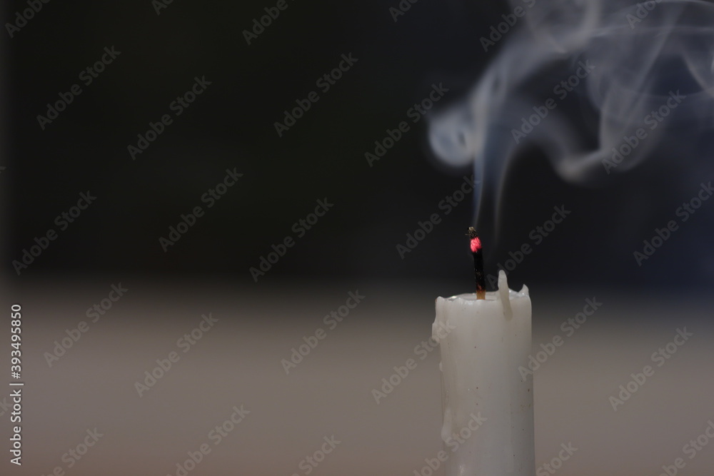 A white candlestick that was extinguished and smoke emitted from the candle flame on a black background. A white candlestick that was extinguished and smoke emitted from the candle flame on a black background.