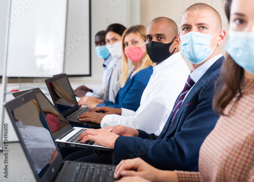 Side view of managers group in protective masks working at laptops in company office