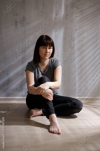 portrait of young thoughtful woman sitting on the floor with shadow from the blinds