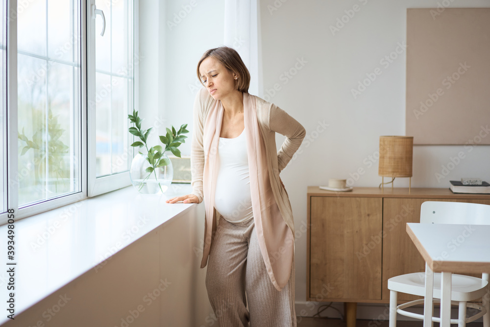 Healthcare, treatment. Young pregnant woman feeling sudden pain in her back. Future mom suffering from backpain. High quality photo