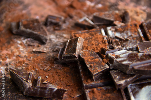 Dark chocolate bar with chocolate pieces with cocoa powder on brown background, close-up view