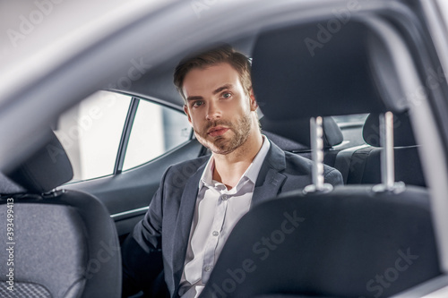 Serious brown-haired male sitting at backseat of car © zinkevych