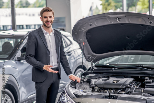 Smiling brown-haired male pointing at open car hood