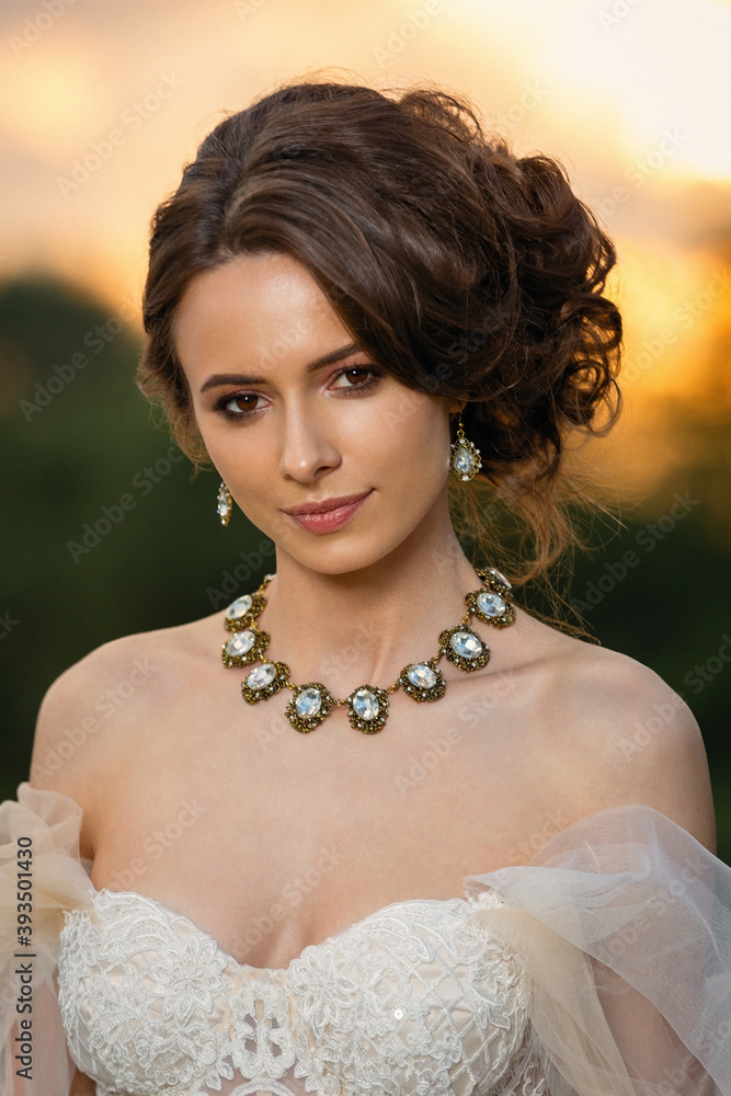 portrait of a beautiful girl in a white wedding dress in summer on a sunset background