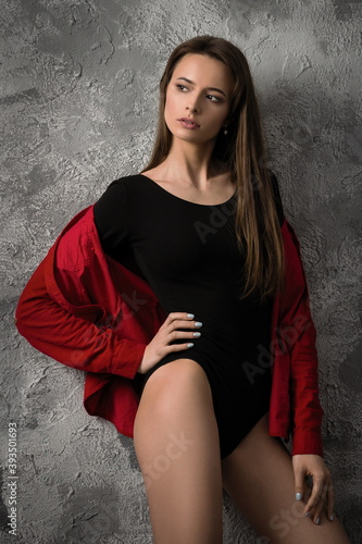 beautiful slender model in black bodysuit and red shirt posing against the background of an old wall