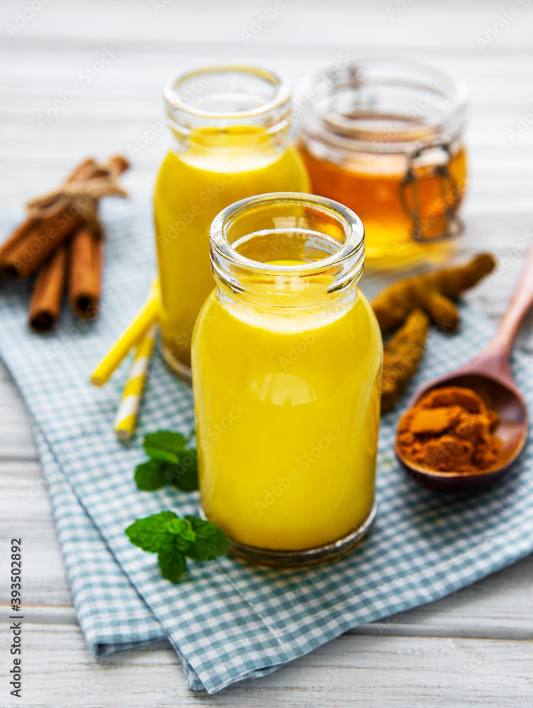 Yellow turmeric latte drink. Golden milk with cinnamon, turmeric, ginger and honey over white wooden background. Yellow turmeric latte drink. Golden milk with cinnamon, turmeric, ginger and honey over white wooden background.
