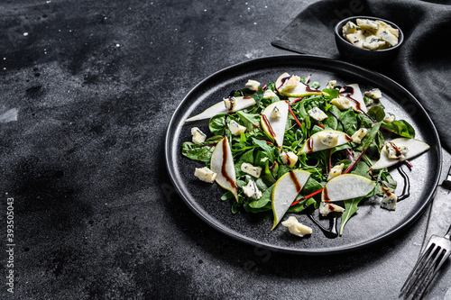 Pear, blue cheese, arugula and nut salad on plate. Black background. Top view. Copy space