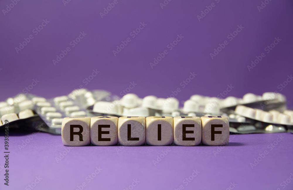 The word relief written with wooden dices in front of a purple background and drugs tablets The word relief written with wooden dices in front of a purple background and drugs tablets