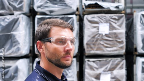 Logistics Engineer Warehouse Worker Walking Past Shelves Full Industrial Goods and Products Packed For Shipping. Industry Workman Mechanic Foreman Wearing Safety Uniform In Factory Plant Storage.