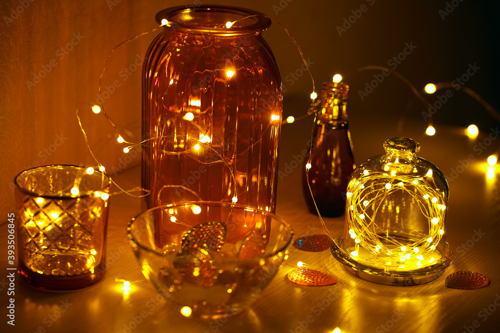 Glass vases, jars and candlesticks with led lights on a wire. Cozy details of home decor. Christmas decorations on the table. Glass vases, jars and candlesticks with led lights on a wire. Cozy details of home decor. Christmas decorations on the table.