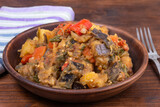 Traditional Italian vegetable stew with potatoes, eggplants, tomatoes and peppers in a rustic earthen plate on a rustic background - Neapolitan style cianfotta.