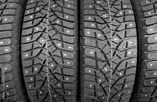 Winter studded tire. Winter car tires background. Tire stack background. Tyre protector close up. Square powerful spikes. Black studdable winter tyre profile. Car tires in a row