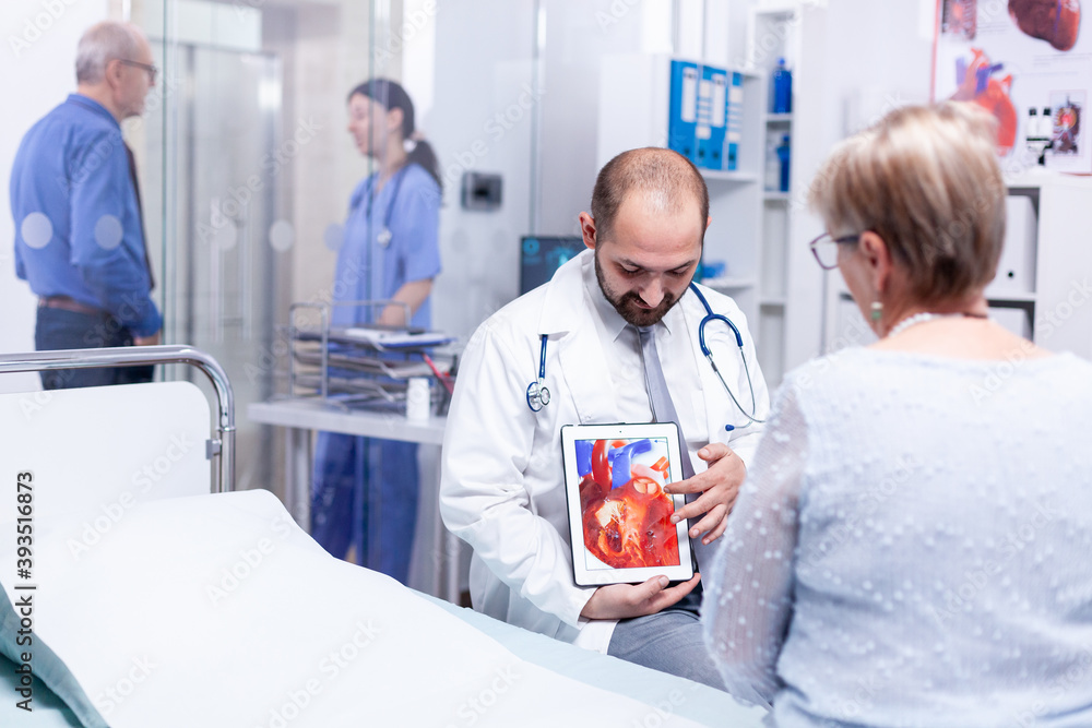 Obraz premium Physician pointing at heart disease using tablet pc and talking with patient about diagnosis. Medical services medicine healthcare well-being support, physician working