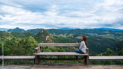 Portrait image of a female traveler sitting and looking at a beautiful mountain and nature view