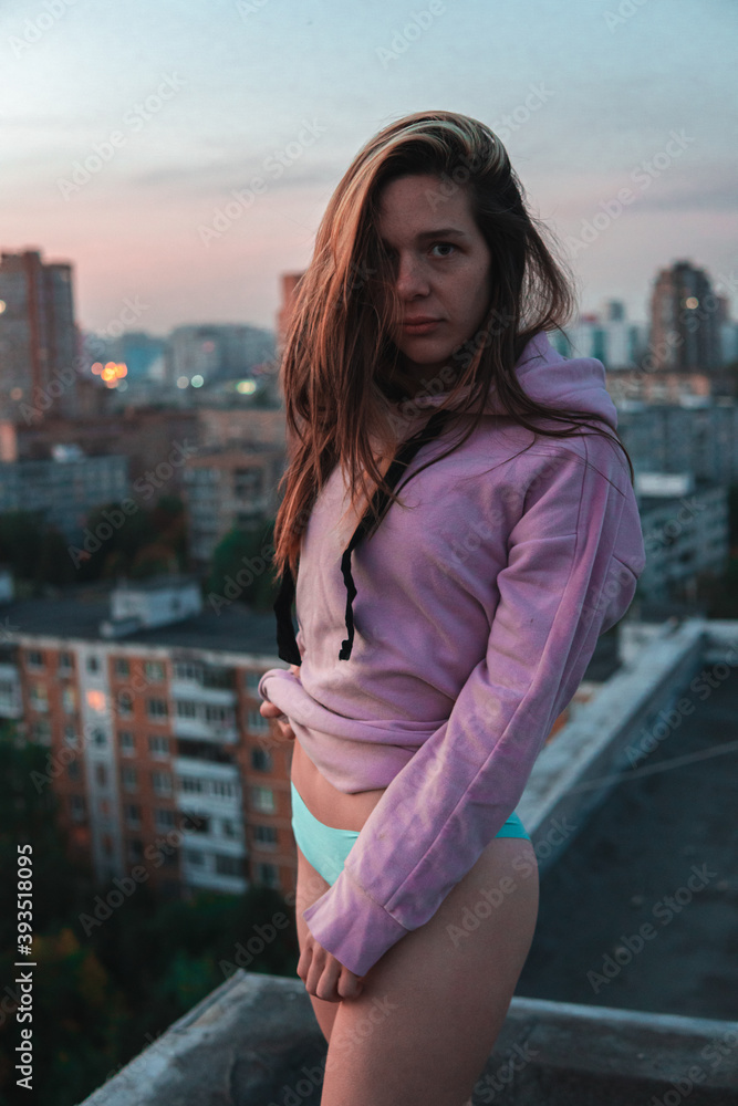 girl in pink hoodie and panties posing on the rooftop during sunset