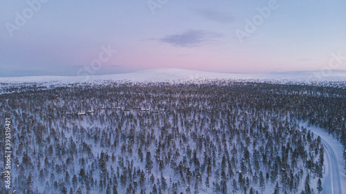 Winter sunset in Lapland, Arctic circle. Moon rising over horizon. Aerial drone shot of the forest covered in snow winter and the village inside the Arctic Circle. Lapland, Finland. Winter sunrise 