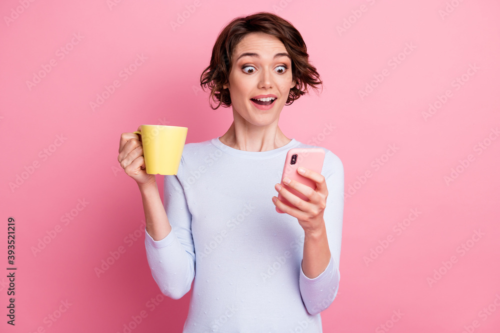 Positive astonished girl hold mug beverage use smartphone wear white jumper isolated pastel color background Positive astonished girl hold mug beverage use smartphone wear white jumper isolated pastel color background