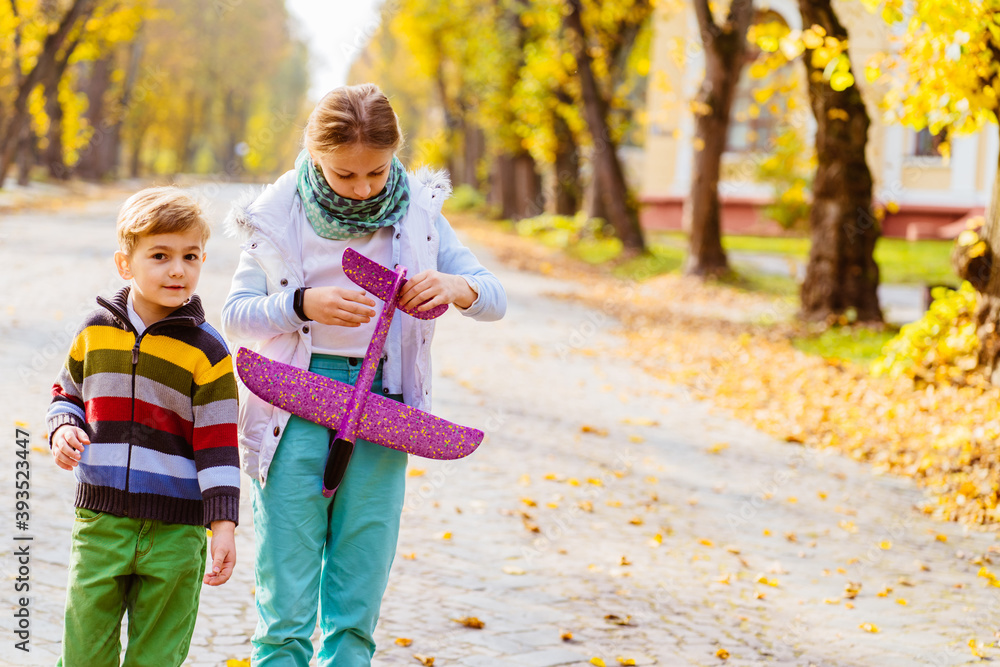 Group portrait of two white caucasian children kids, older sister and younger brother playing planes on city park outdoors, happy lifestyle childhood concept. Group portrait of two white caucasian children kids, older sister and younger brother playing planes on city park outdoors, happy lifestyle childhood concept.
