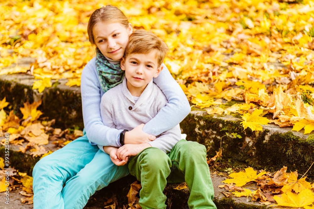 Portrait of adorable happy sister and brother in fashionable coats hugs outdoor at a beauty autumn day