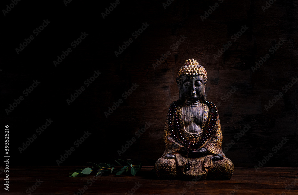 Close up of a statue of Buddha with singing bowl and prayer beads (mala) for chanting mantras as decoration on an old wooden board - yoga