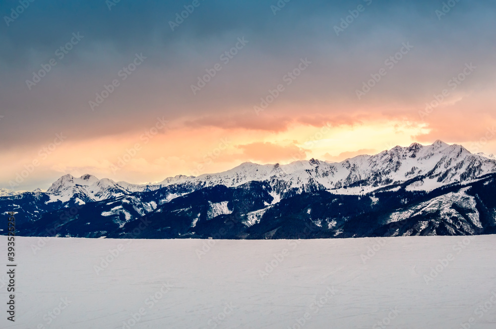 Zell am See in winter. View from Schmittenhohe, snowy slope of ski resort in the Alps mountains, Austria. Stunning landscape with mountain range, snow and sunset sky near Kaprun
