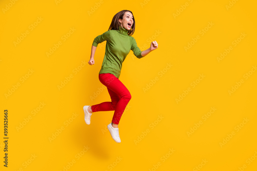 Full size photo of funny lady jump up rushing excited wear casual green pullover shoes red trousers isolated yellow color background