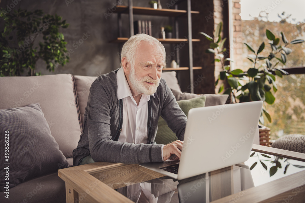 Photo of handsome old man dressed white shirt sitting sofa looking typing modern device indoors flat home house Photo of handsome old man dressed white shirt sitting sofa looking typing modern device indoors flat home house