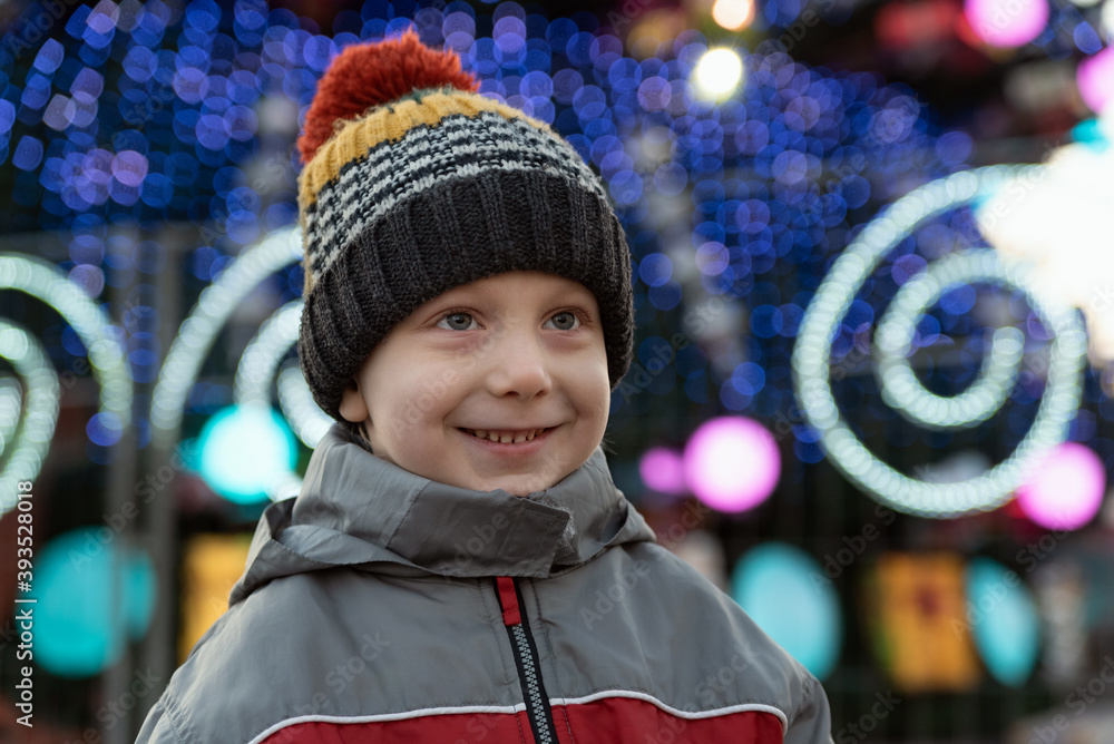 Portrait of boy in warm hat against the background of Christmas tree decorations on the street Portrait of boy in warm hat against the background of Christmas tree decorations on the street