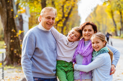 Portriat of family walking outdoors in autumn park against blurred leaves background. Family, leisure love, relation, good mood concept.