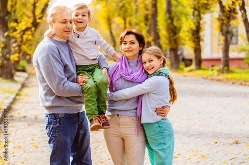 Happy portrait family of four walking in autumn city park. Children and parents posing, hugging, smiling, playing and having fun. Bright yellow trees.