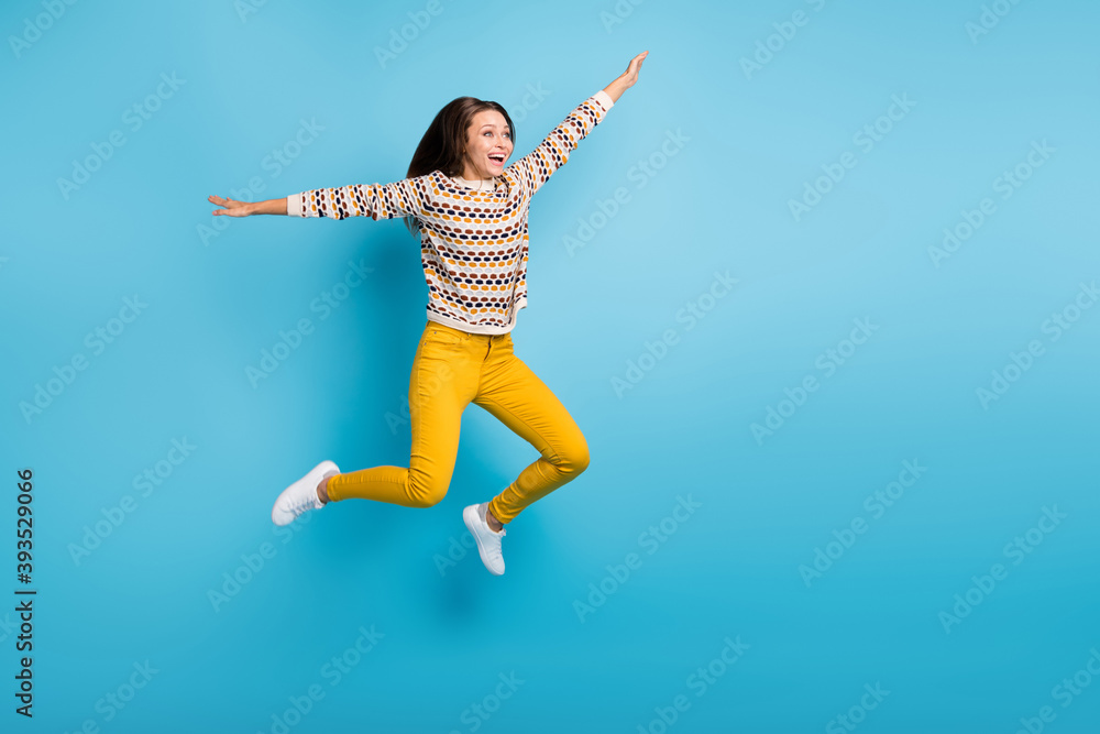 Full length photo of carefree young lady wear ornament sweater jumping hands arms sides isolated blue color background