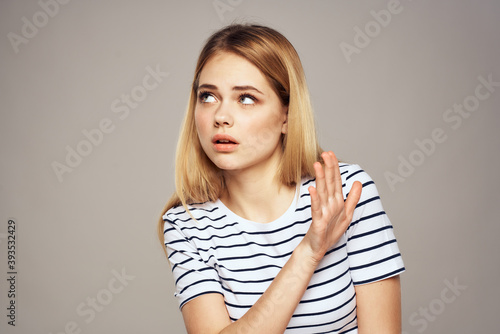 A woman with a displeased expression is gesturing with her hands T-shirt gray background 