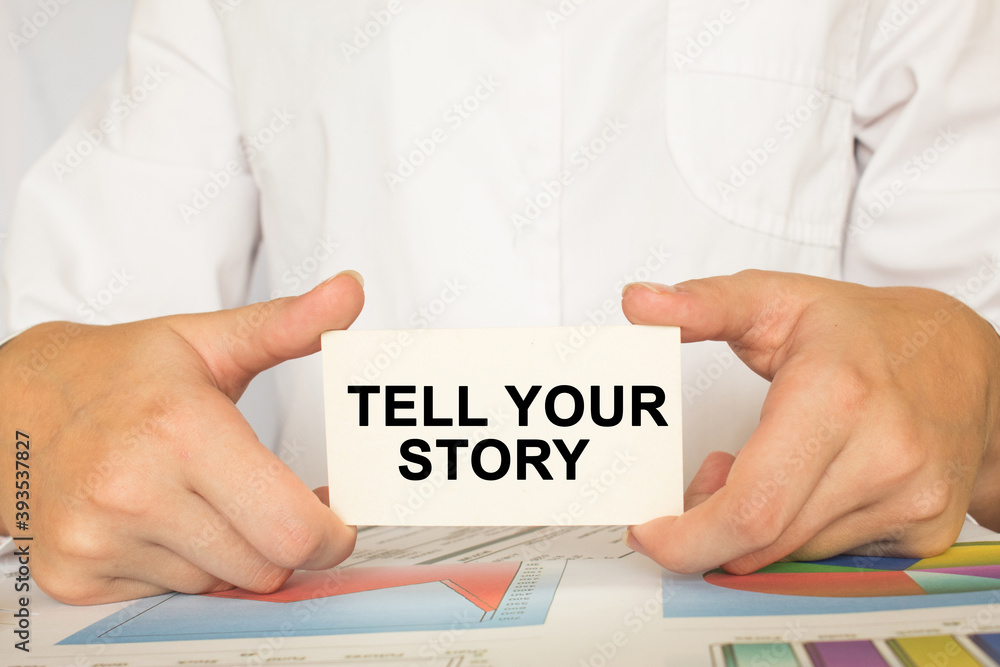 a man in the office holds a card with text TELL YOUR STORY. business concept a man in the office holds a card with text TELL YOUR STORY. business concept