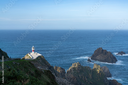 Cabo Ortegal lighthouse in Galicia with green cliffs and sunlight and deep blue ocean