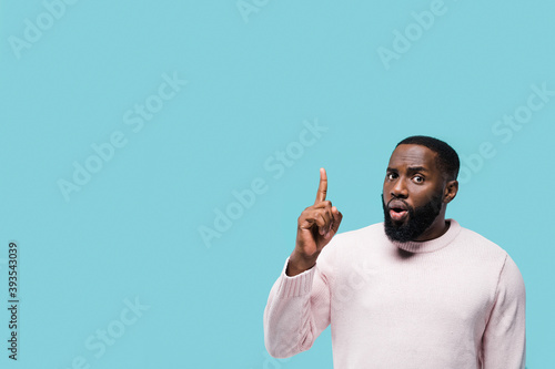 Excited surprised african american man points for finger up on copy space for your advertising or text while standing against blue isolated background
