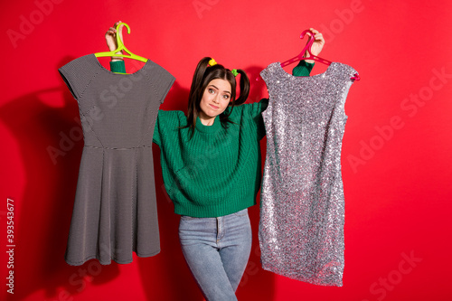 Canvas Print Photo of young attractive doubtful unsure female hold two dresses can't choose i